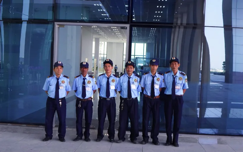 Bảy nhân viên bảo vệ đứng trước cửa kính sảnh tòa nhà văn phòng