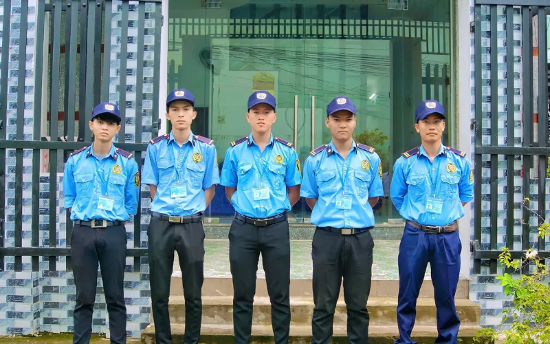 Năm nhân viên bảo vệ đứng trước cổng sắt của tòa nhà